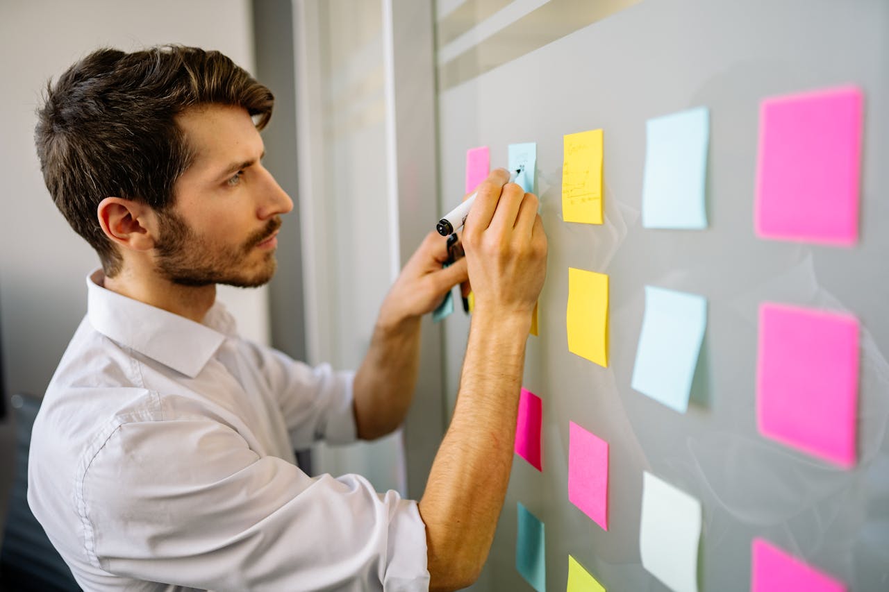 Focused businessman writing on sticky notes in a modern office environment.